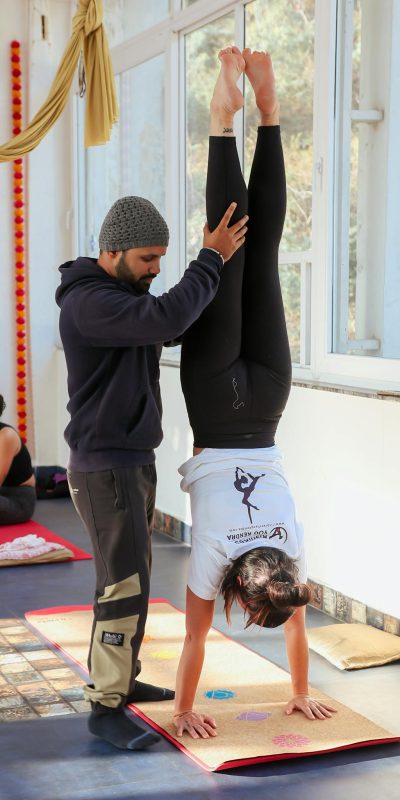 Yoga instructor helps student with handstand in peaceful studio setting.